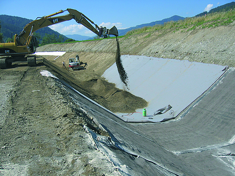 An excavator is moving earth onto the clay sealing membranes