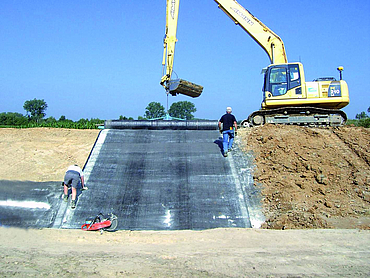 Installation of a clay sealing membrane by staff and an excavator.