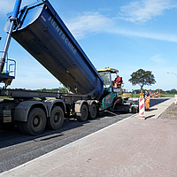 Dump truck dumps asphalt into a term machine for asphalting a road with SamiGrid® composite material