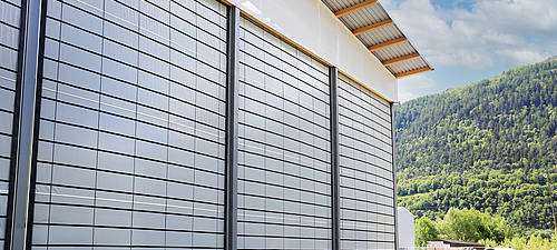 Tectura folding front 3 large folding fronts on a warehouse. Planted mountains and a blue sky can be seen in the background.