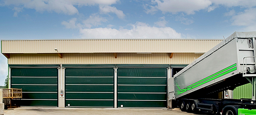 Lubratec Stabitore Three closed green Lubratec Stabitore at a beige warehouse. A truck is being unloaded at the open gate on the right.