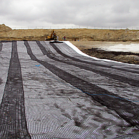 Rolling out Basetrac Grid geogrid with a spreader bar for base course reinforcement on a construction site