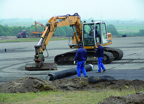 Excavators and workers laying geosynthetic clay liners
