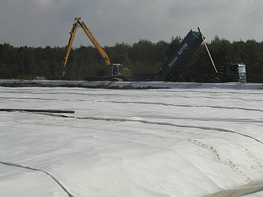A long-reach excavator is spreading earth
